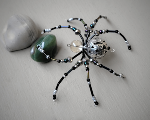 Beaded wire spider featuring a detailed silver-patterned bead, black legs, and shimmering accent beads for a mystical handmade décor piece.